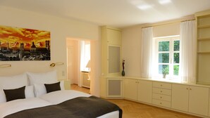 A bedroom with a large bed, a window with curtains, a painting on the wall, and a wardrobe. - Residenz am englischen Garten (Munich)