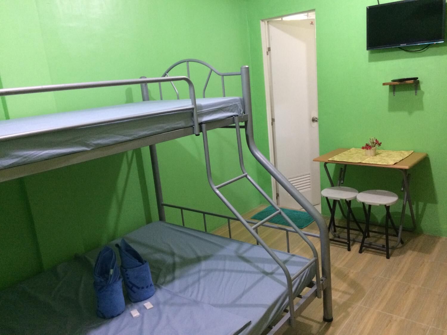 Una cama litera con escritorio y dos sillas, un televisor y una puerta en una habitación de paredes verdes.