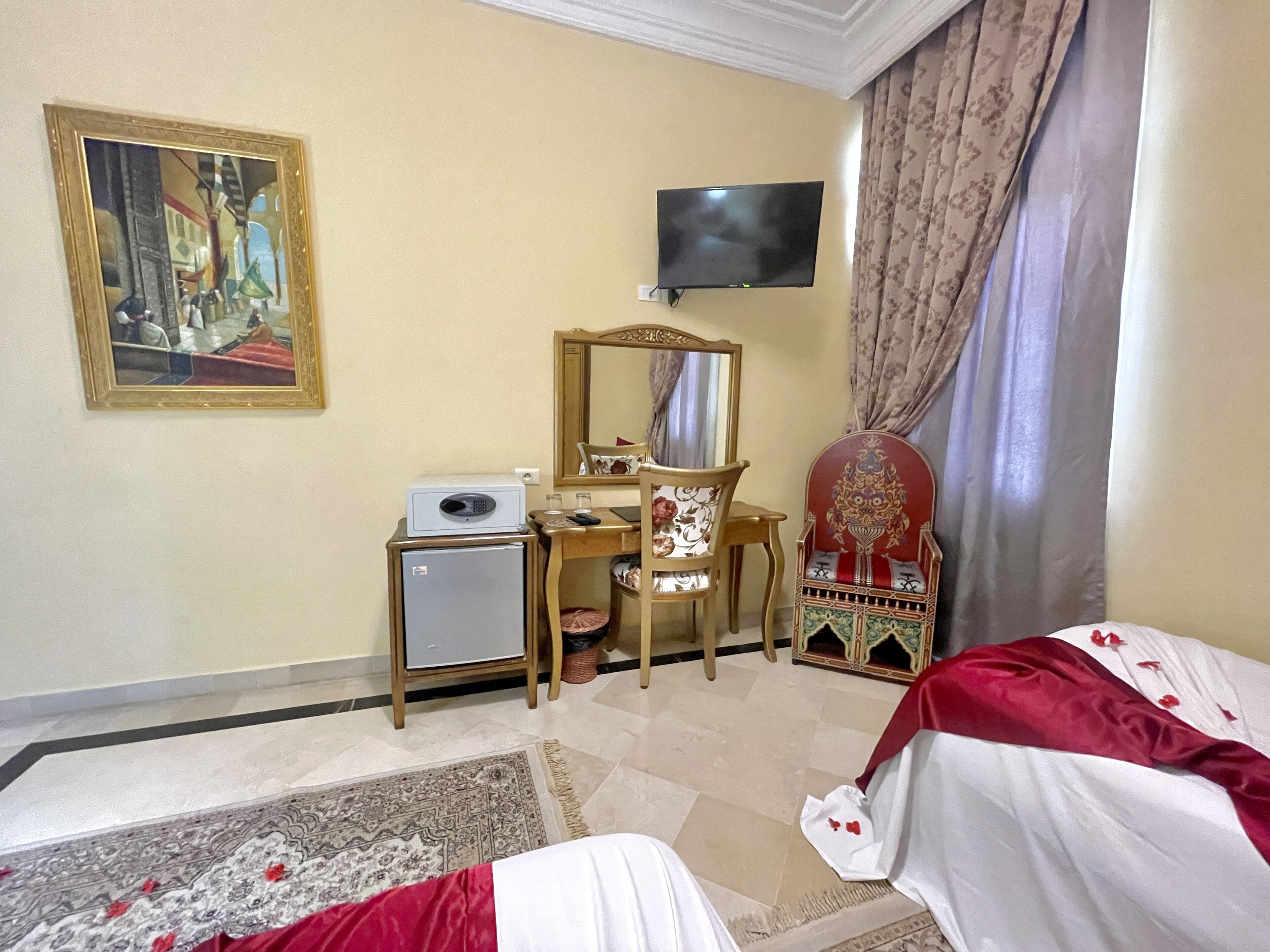 Habitación de hotel con cama, escritorio con computadora, televisor, espejo y refrigerador pequeño.