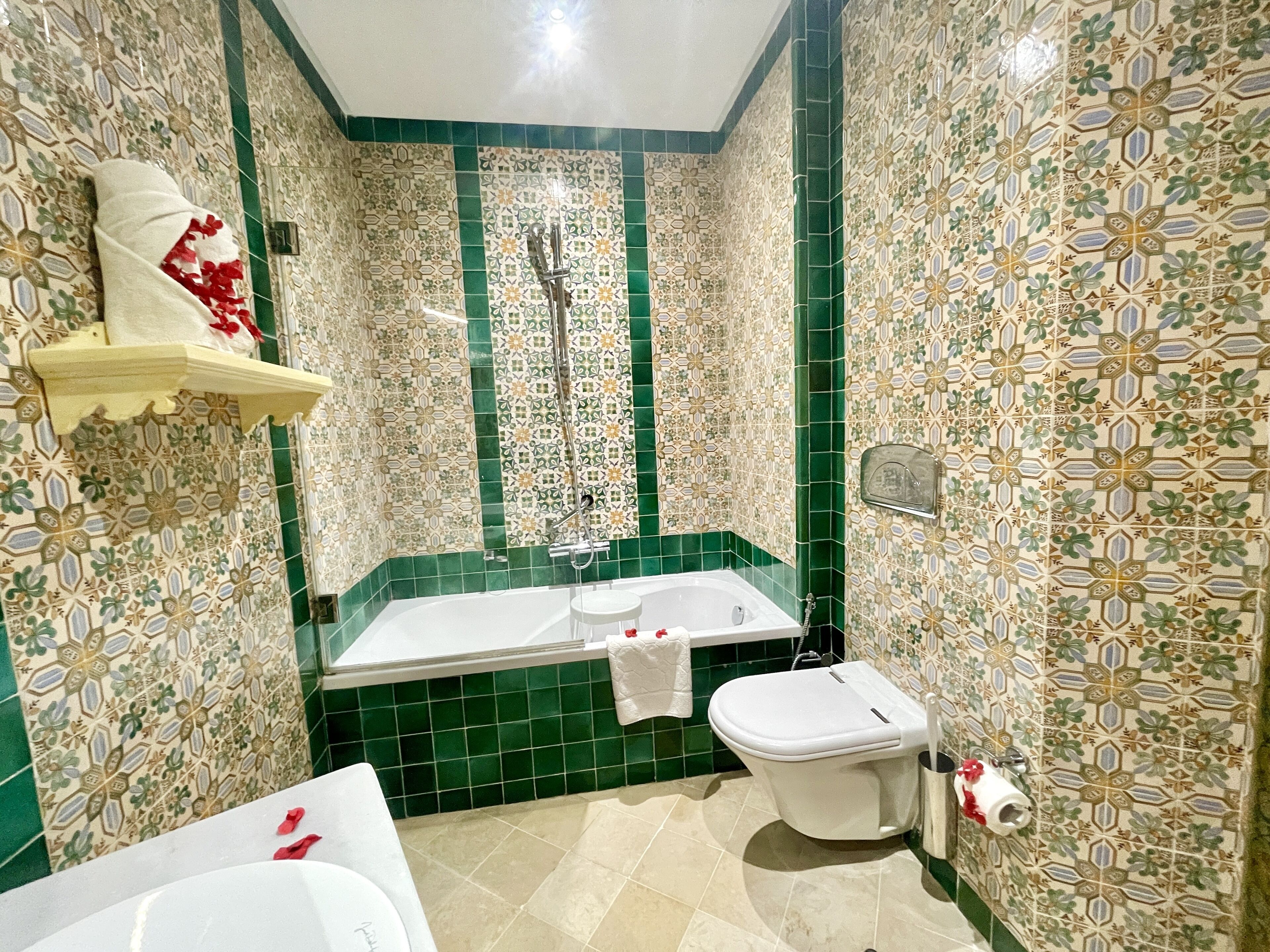 Un baño con bañera, inodoro y lavamanos, con baldosas decorativas verde y beige.