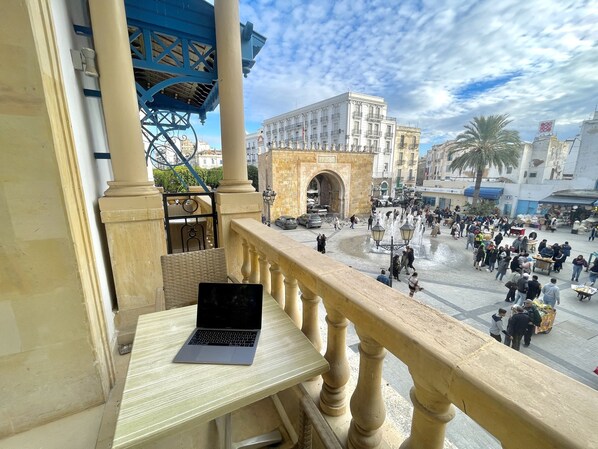 A balcony with a laptop, overlooking a busy public square with a historic archway and people. - Royal Victoria - Ex British Embassy (Tunis)