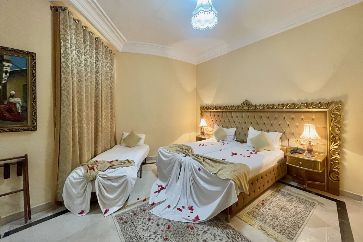 A hotel room with two beds, a chandelier, a painting, and a patterned rug.