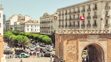A busy urban street with a prominent stone archway and a flag on a building.