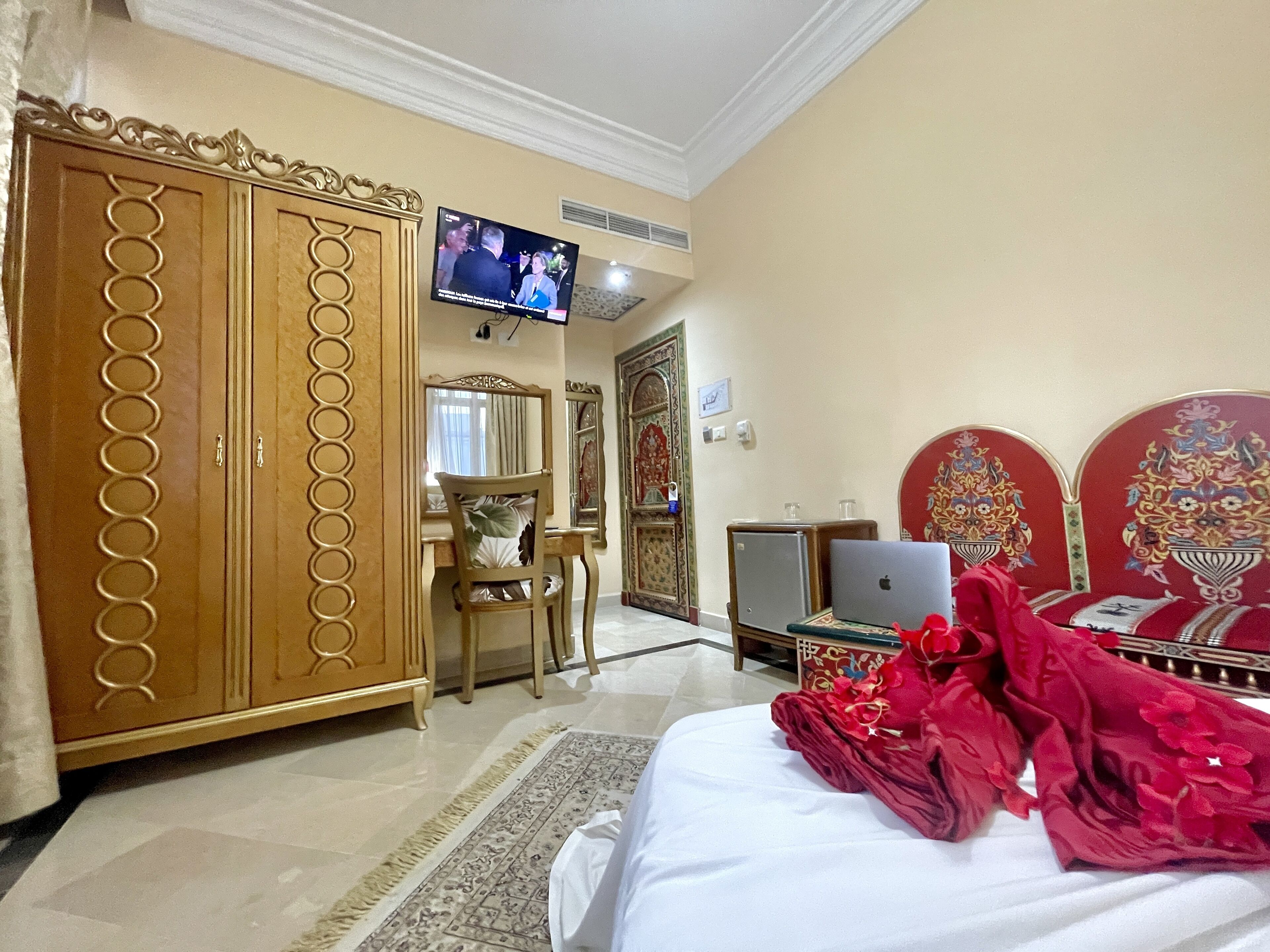 Habitación de hotel con una cama grande, un armario, un escritorio con una computadora portátil, un televisor y un espejo decorativo.