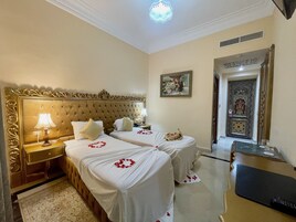 A hotel room with two beds, a nightstand, a lamp, a painting, and a door with intricate designs.
