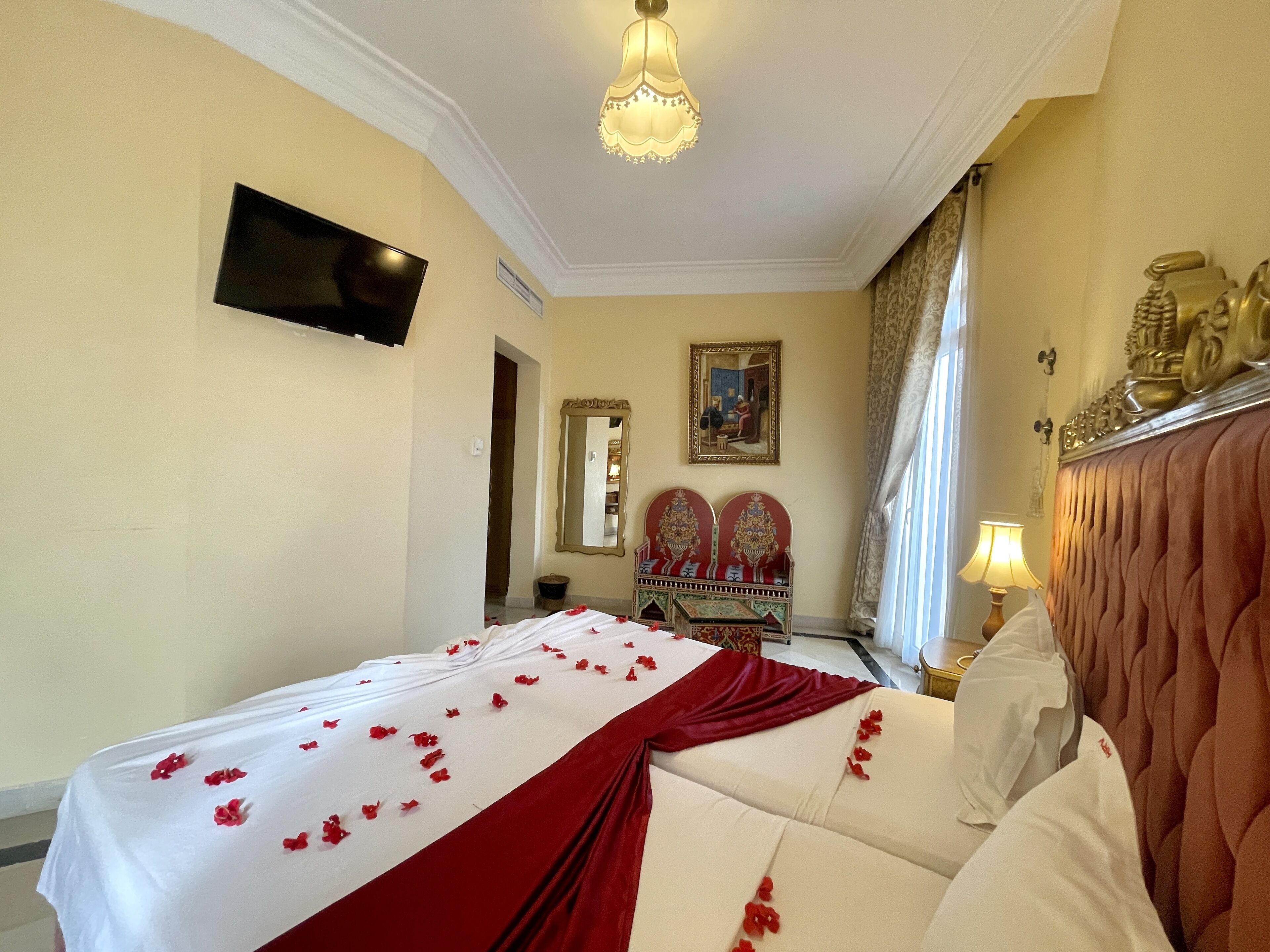 A hotel room with a bed, a television, a mirror, a decorative headboard, and a lamp.