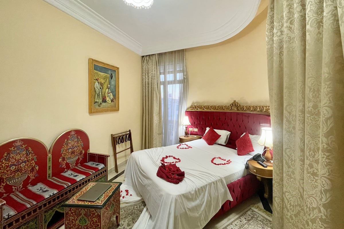 A hotel room with a large bed, a sitting area with a sofa and chairs, a small table, and a nightstand with a lamp.