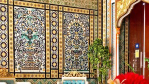A luxurious room with ornate tile walls, a plush blue sofa, a small white table, and a decorative vase with flowers. - Royal Victoria - Ex British Embassy (Tunis)