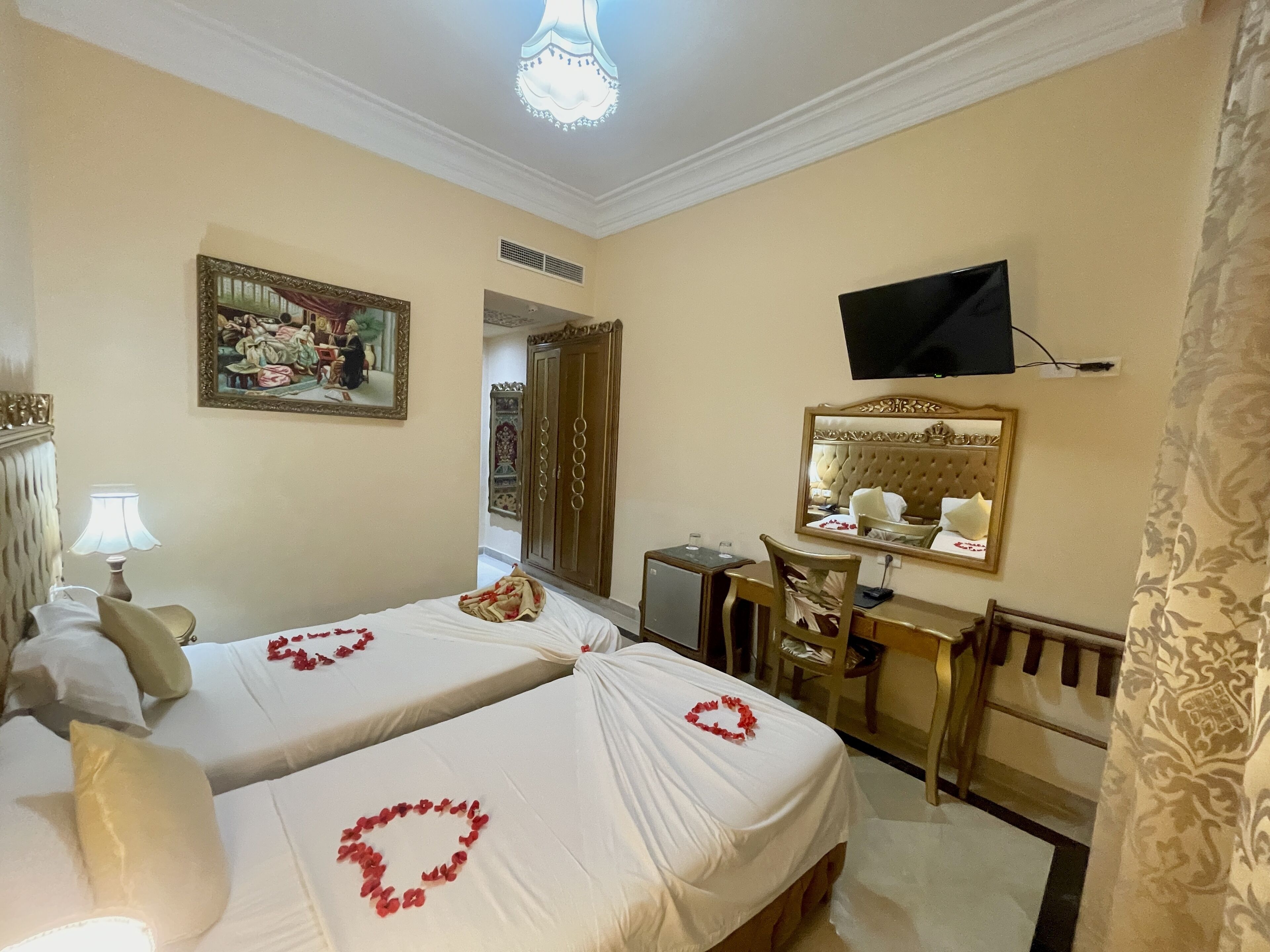 A hotel room with two beds, a desk, a chair, a television, and a mirror.