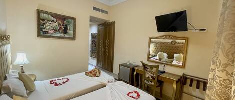 A hotel room with two beds, a desk, a chair, a television, and a mirror.