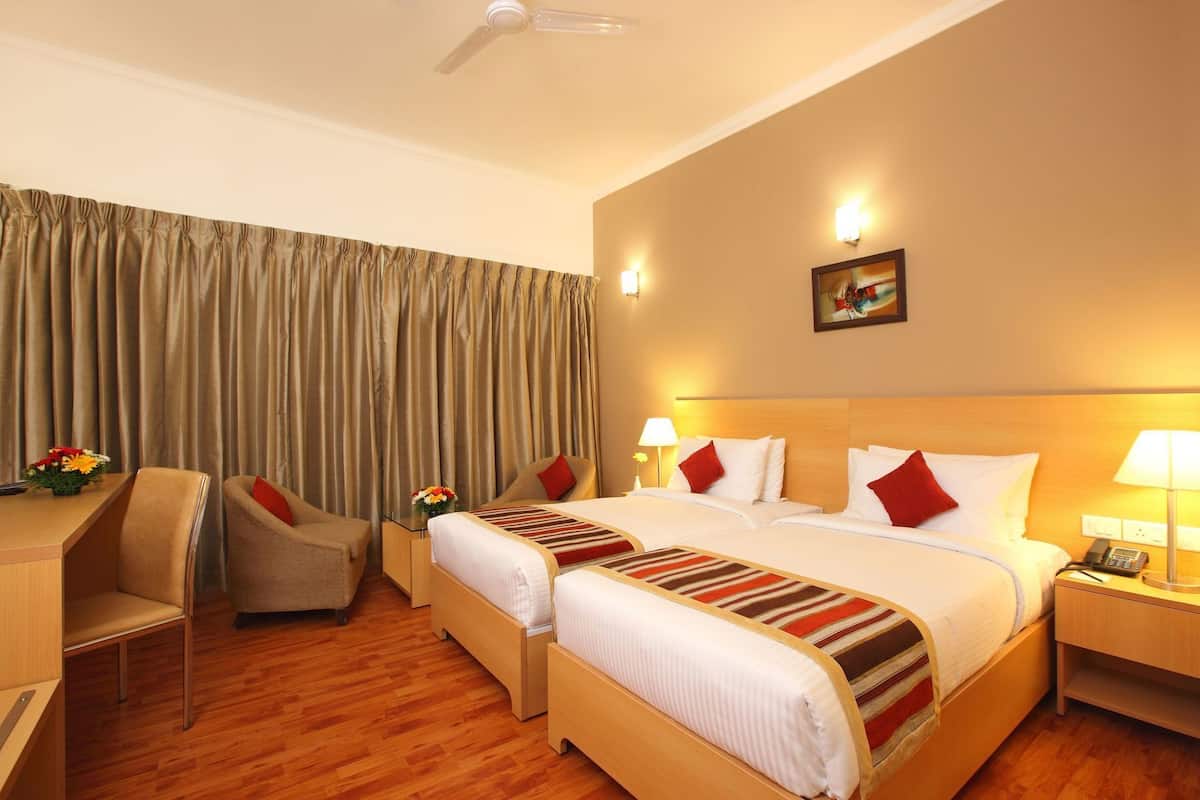 A hotel room with two beds, a desk, a chair, a desk lamp, a phone, and a ceiling fan.