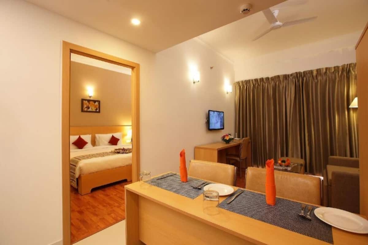 A hotel room with a bed, a desk with a chair, a television, and a dining area with curtains.