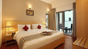 Une chambre d’hôtel avec un grand lit, des lampes de chevet, un téléphone, un tableau au mur et un balcon avec des chaises.
