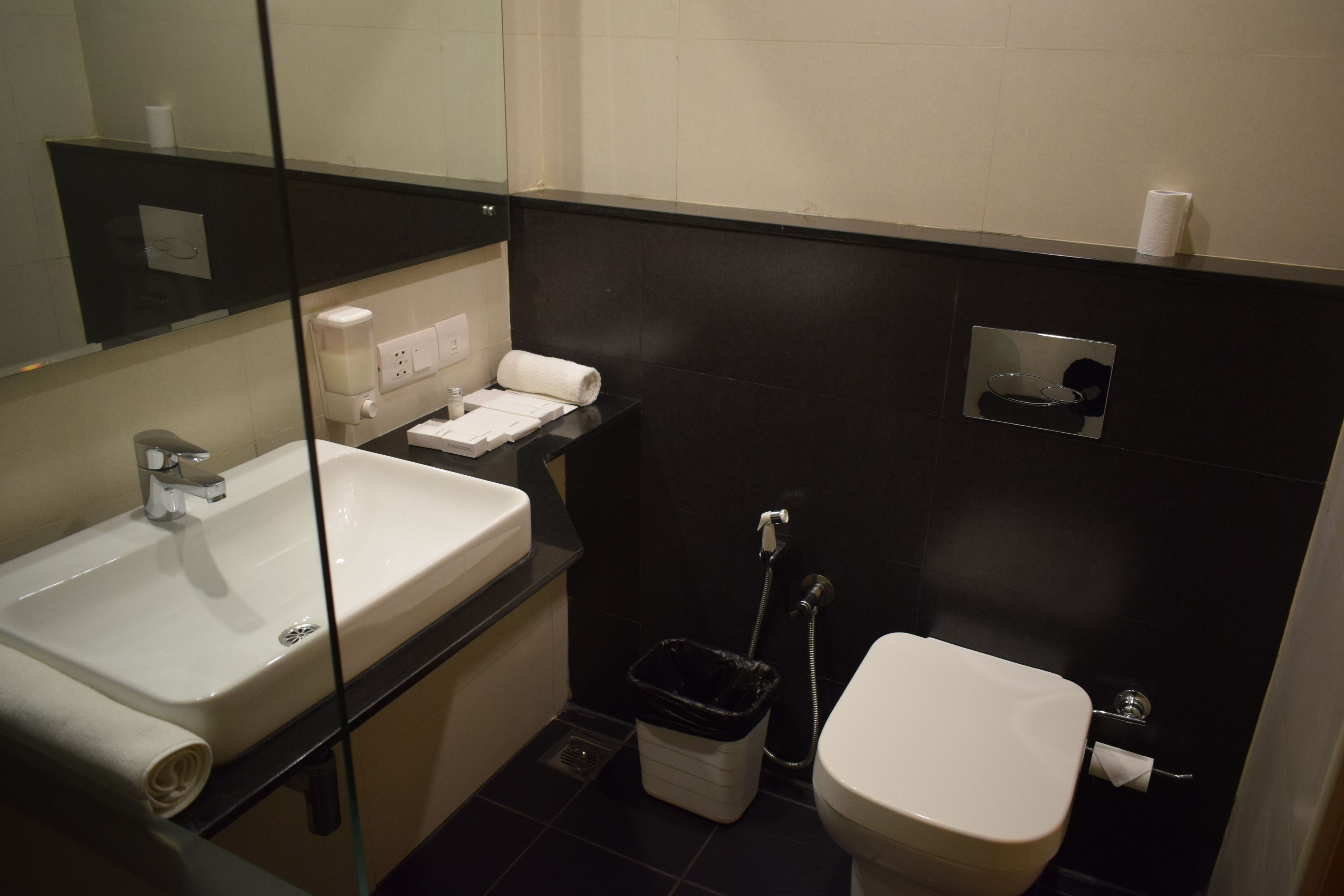 A small, modern bathroom with a white sink, a toilet, and a glass partition.