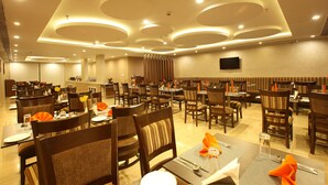 Un vaste espace de salle à manger avec de nombreuses tables et chaises, un téléviseur à écran plat fixé au mur et un design moderne du plafond avec des luminaires encastrés.