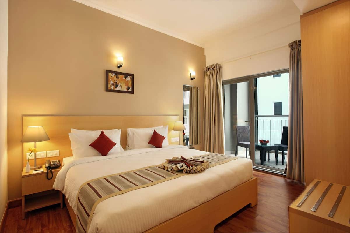 A hotel room with a large bed, bedside lamps, a nightstand, a view of the balcony, and a wooden floor.