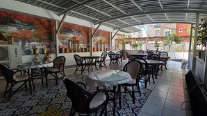 An outdoor cafe with tables and chairs, a tiled floor, and a mural of a waterfall. - Bayindir Palme (Antalya)