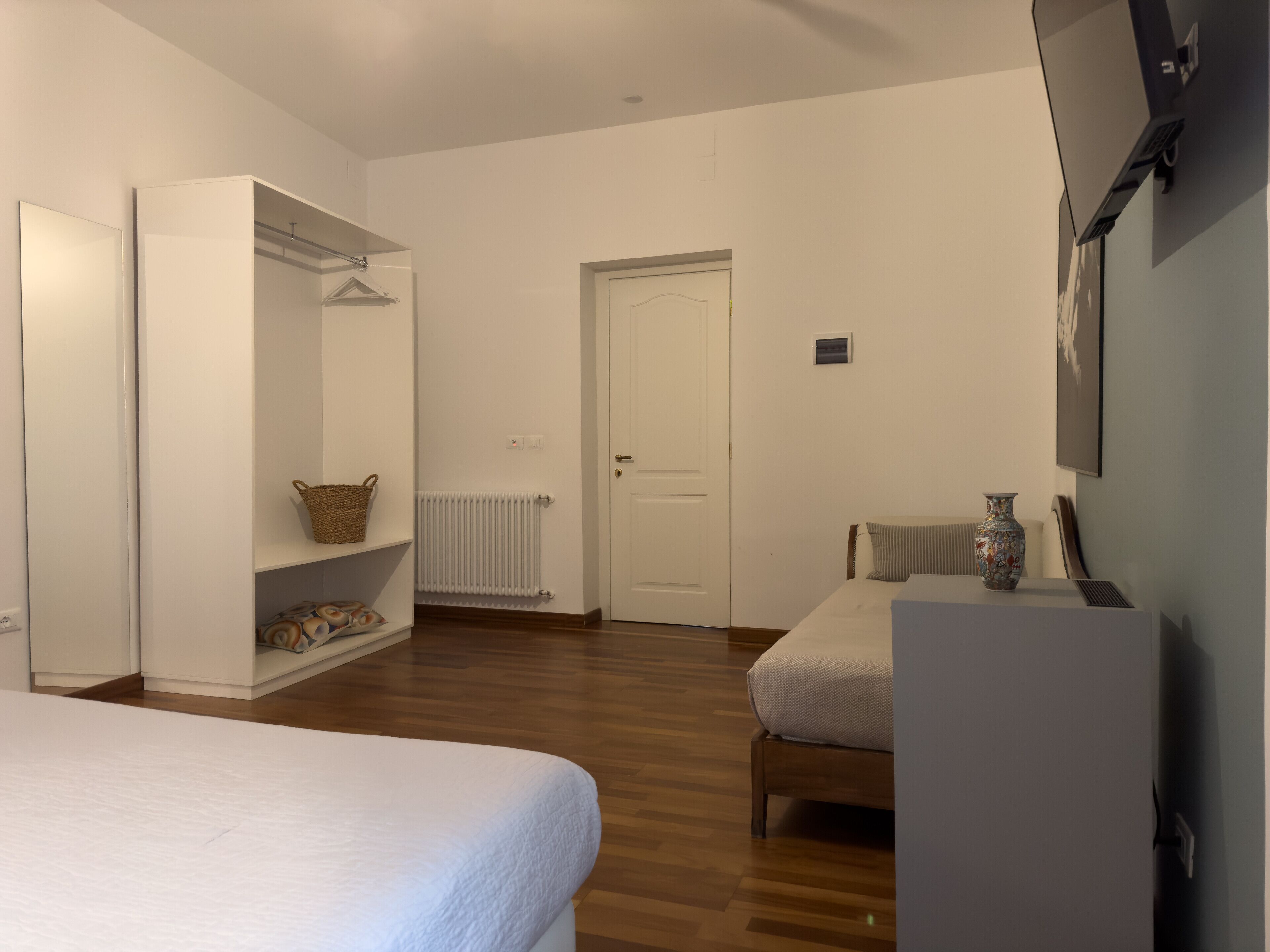 A bedroom with a bed, a wardrobe, a radiator, a door, and a small table with a vase.