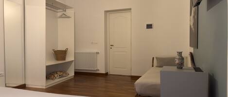 A bedroom with a bed, a wardrobe, a radiator, a door, and a small table with a vase.