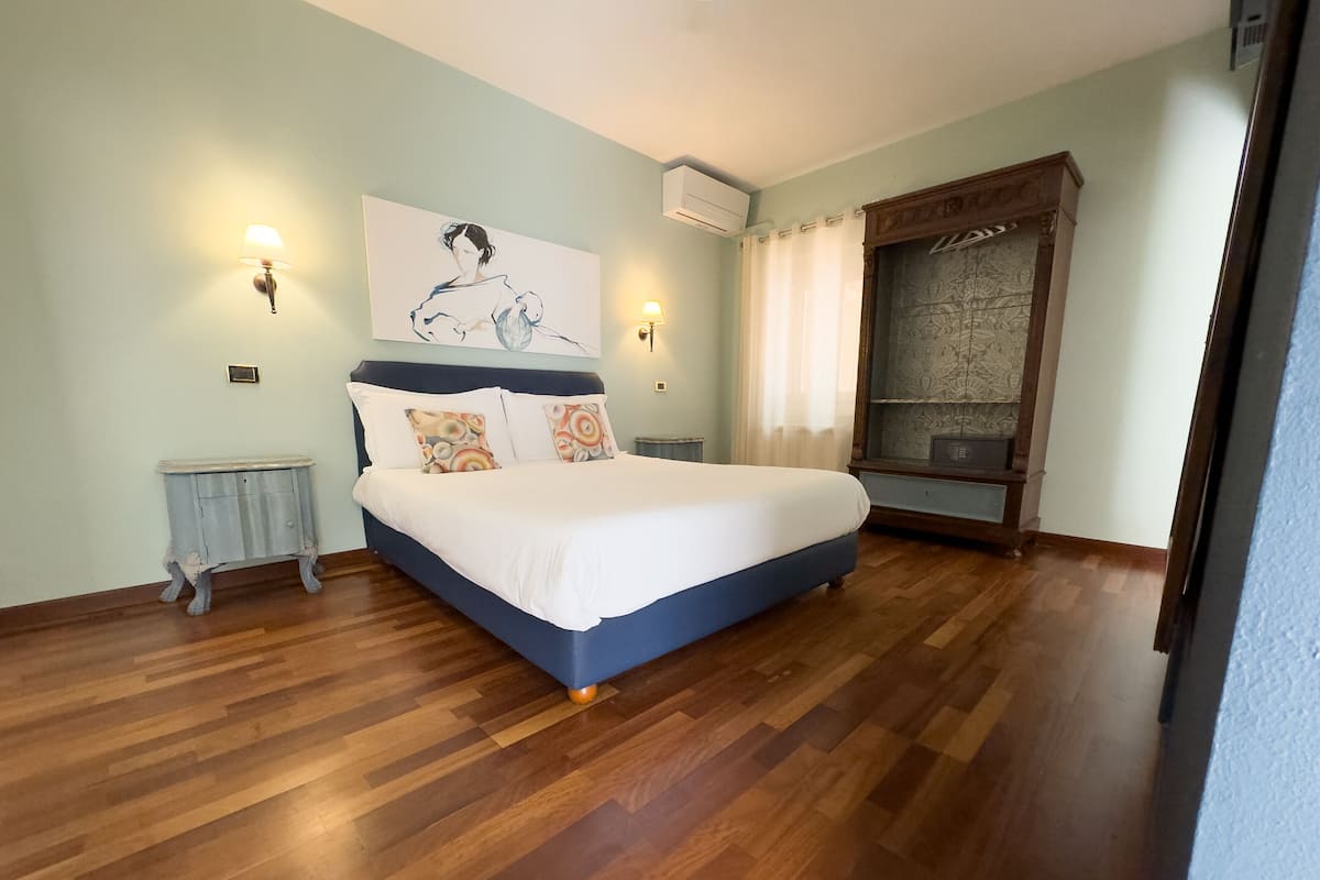 A bedroom with a large bed, two wall-mounted lamps, a radiator, and a window with curtains.