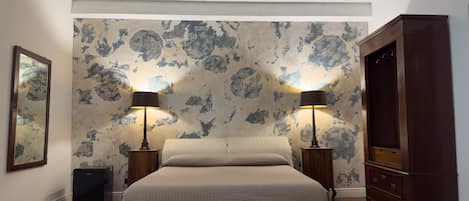 A bedroom with a large bed, two bedside tables with lamps, a wardrobe, and a patterned wallpaper.