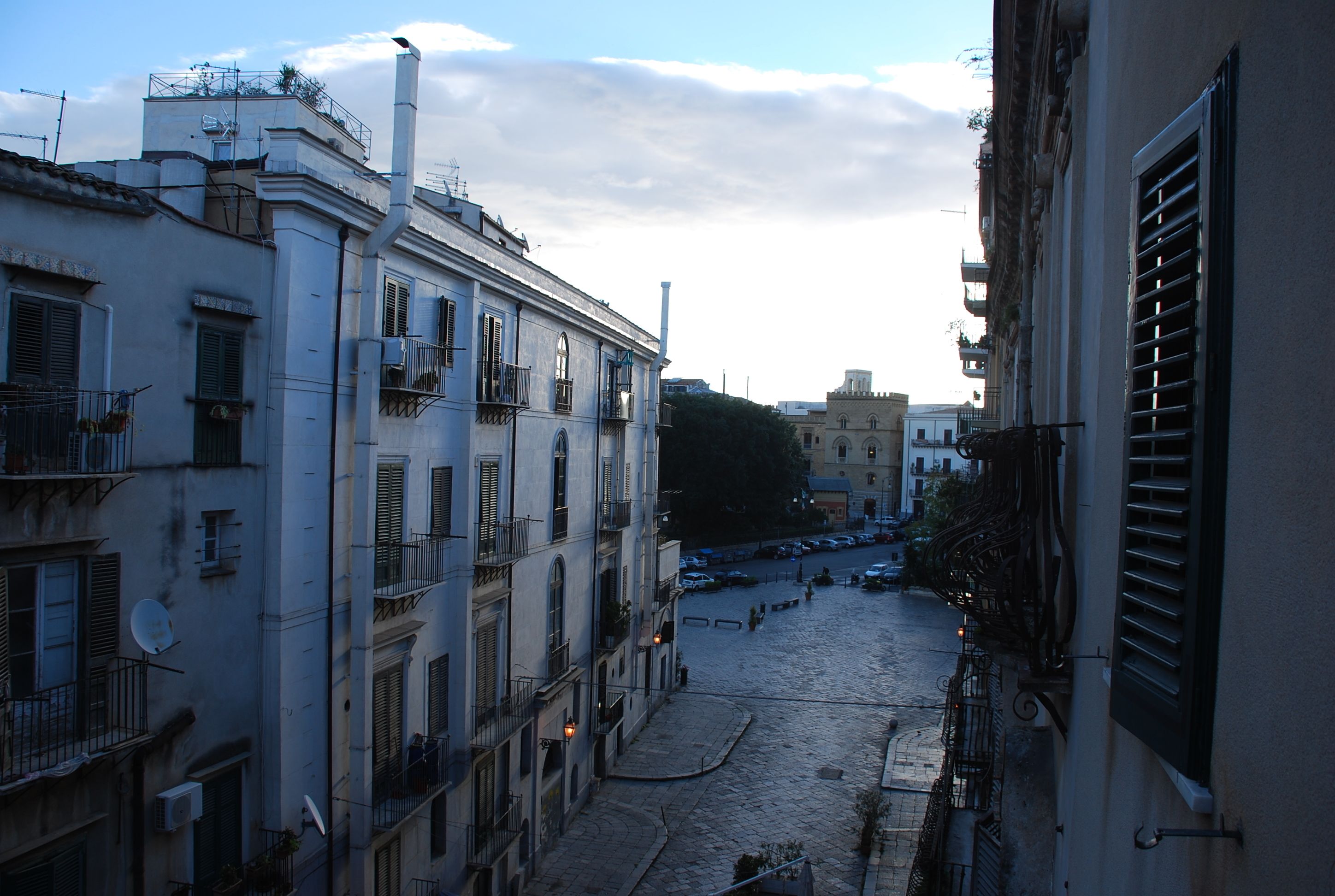 A cobblestone street in a European city with historic buildings, balconies, and a clear sky.