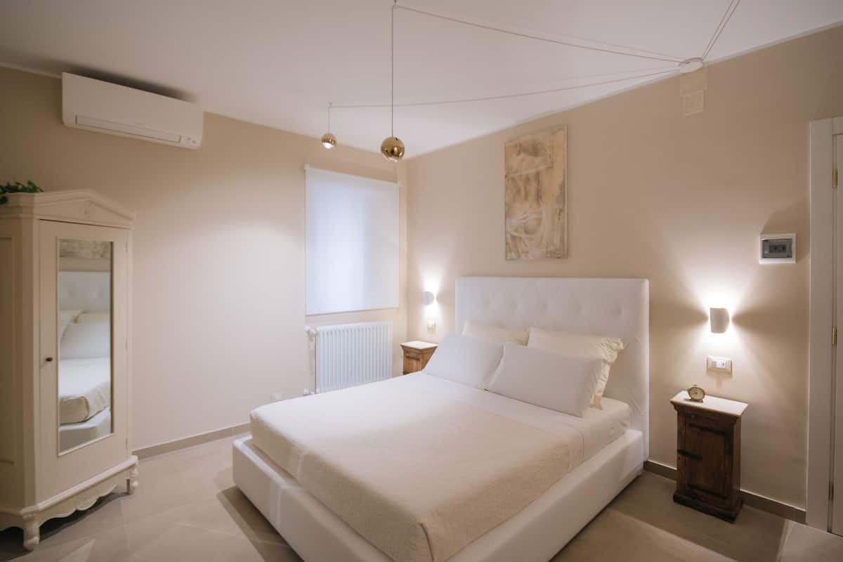 A bedroom with a large bed, a wardrobe, a radiator, and a wall-mounted light fixture.