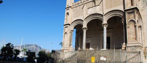 A historic building with a grand entrance, columns, and a staircase leading up to a balcony.