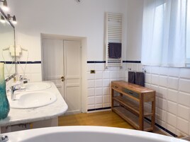 A bathroom with two sinks, a wooden bench, a towel rack, and a window with curtains.