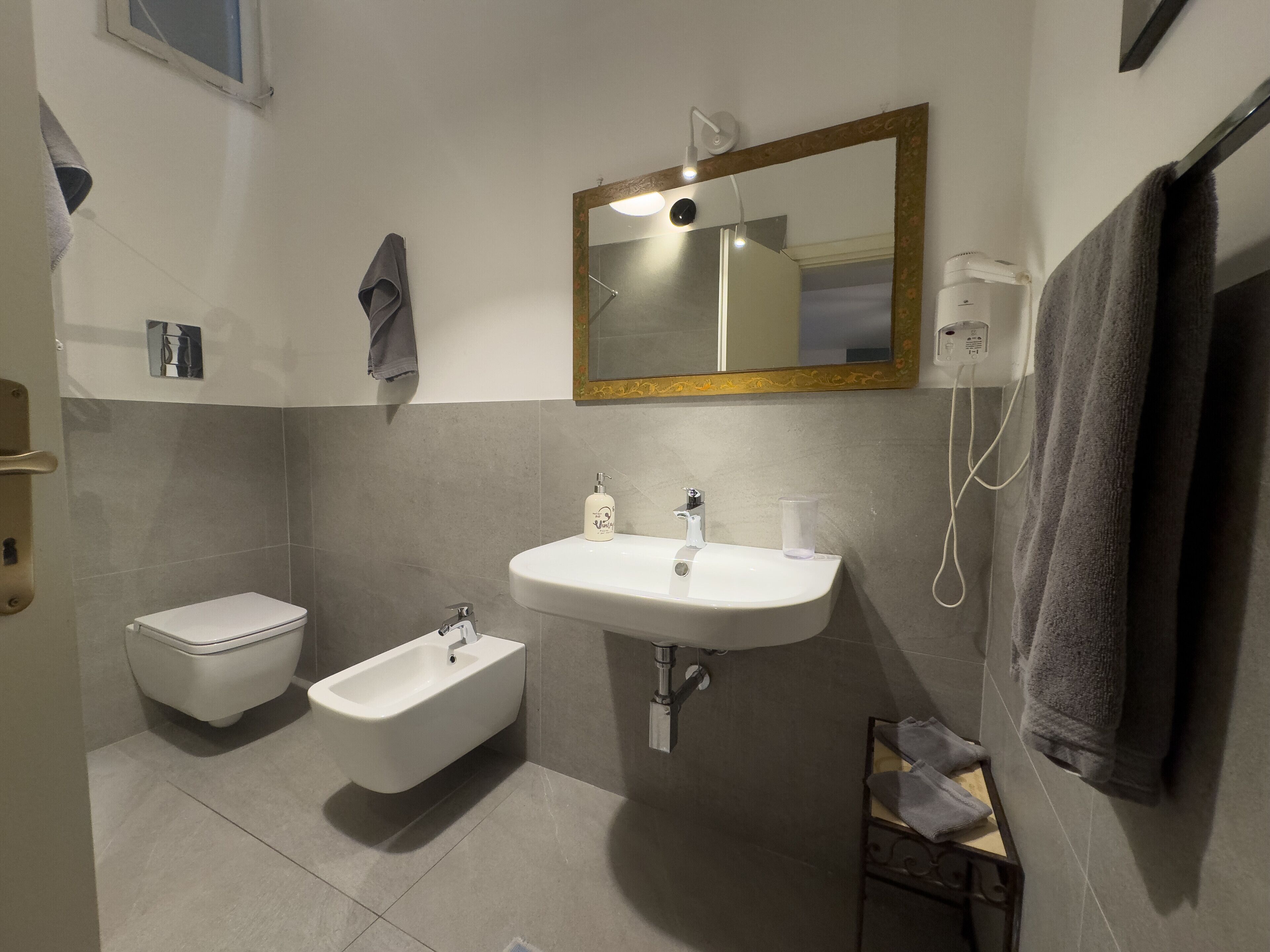 Un bagno moderno con servizi igienici, bidet, lavandino e uno specchio con cornice dorata.
