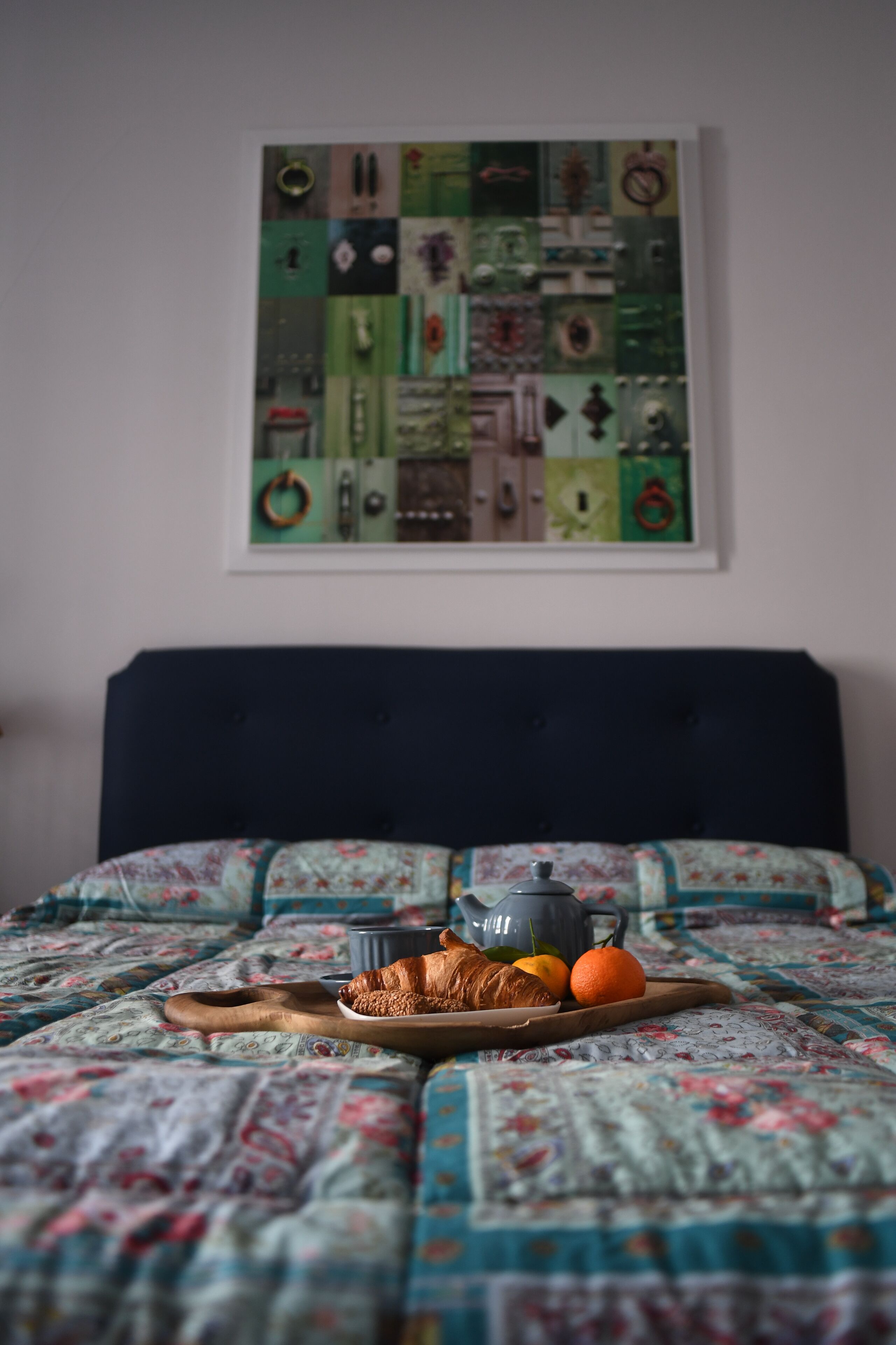 Een bed met een sprei, een dienblad met croissants, sinaasappels en een theepot.