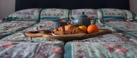 A bed with a quilt, a tray with croissants, oranges, and a teapot.