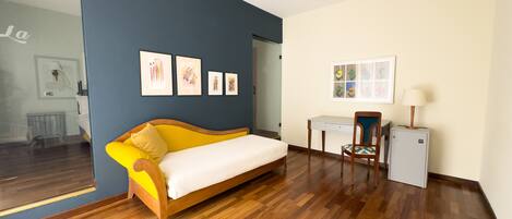 A room with a wooden floor, a yellow sofa, a desk, a chair, and a radiator.