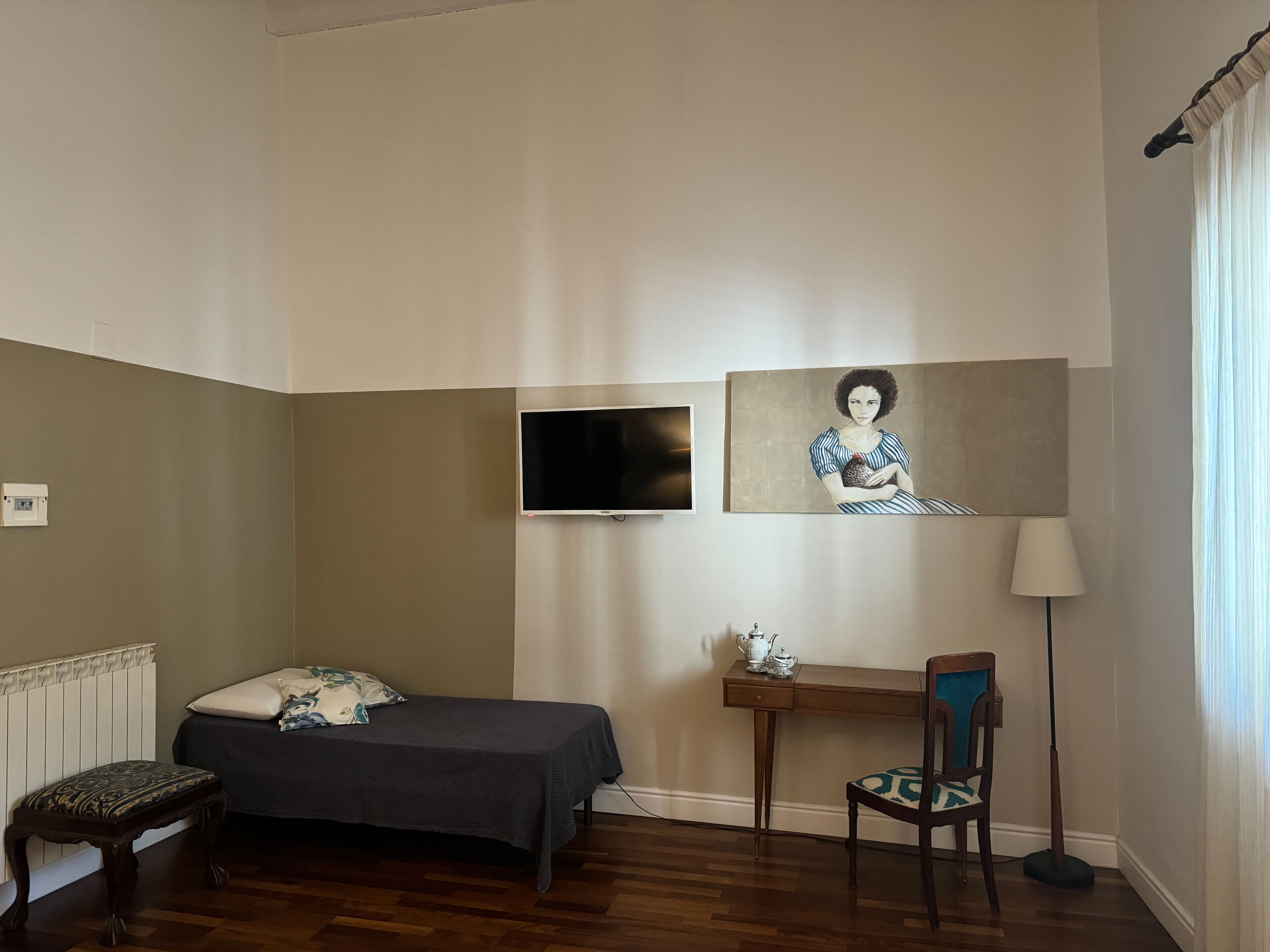 A bedroom with a bed, a desk, a chair, a television, and a painting on the wall.