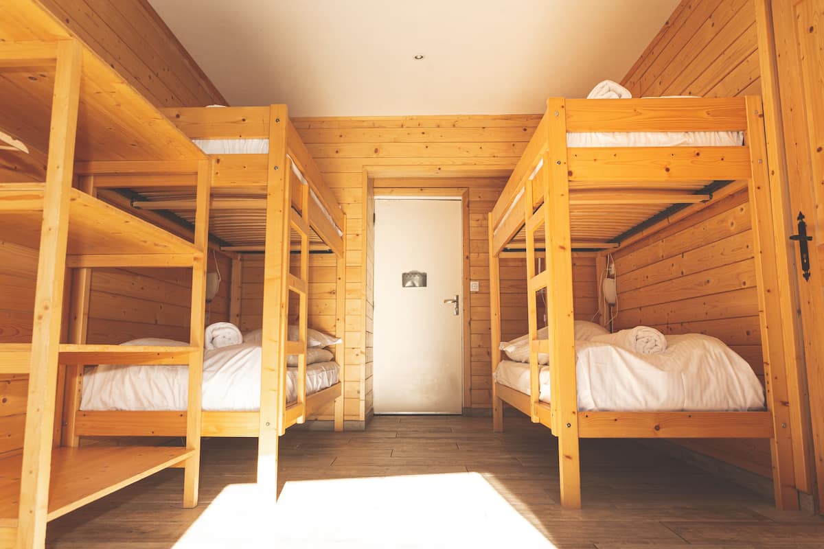A room with three wooden bunk beds, a white door, and a small window.