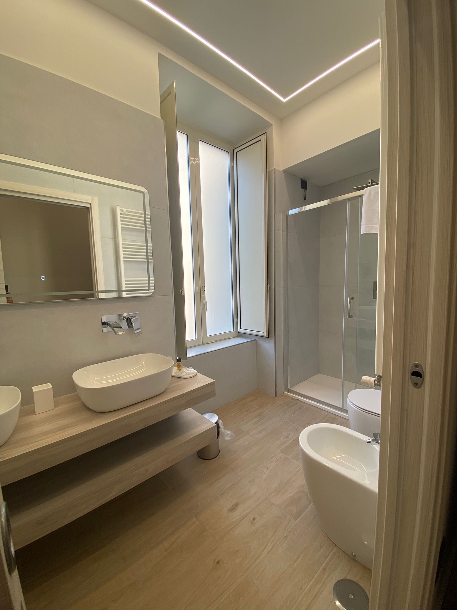 A modern bathroom with a large mirror, two sinks, a bathtub, and a shower.