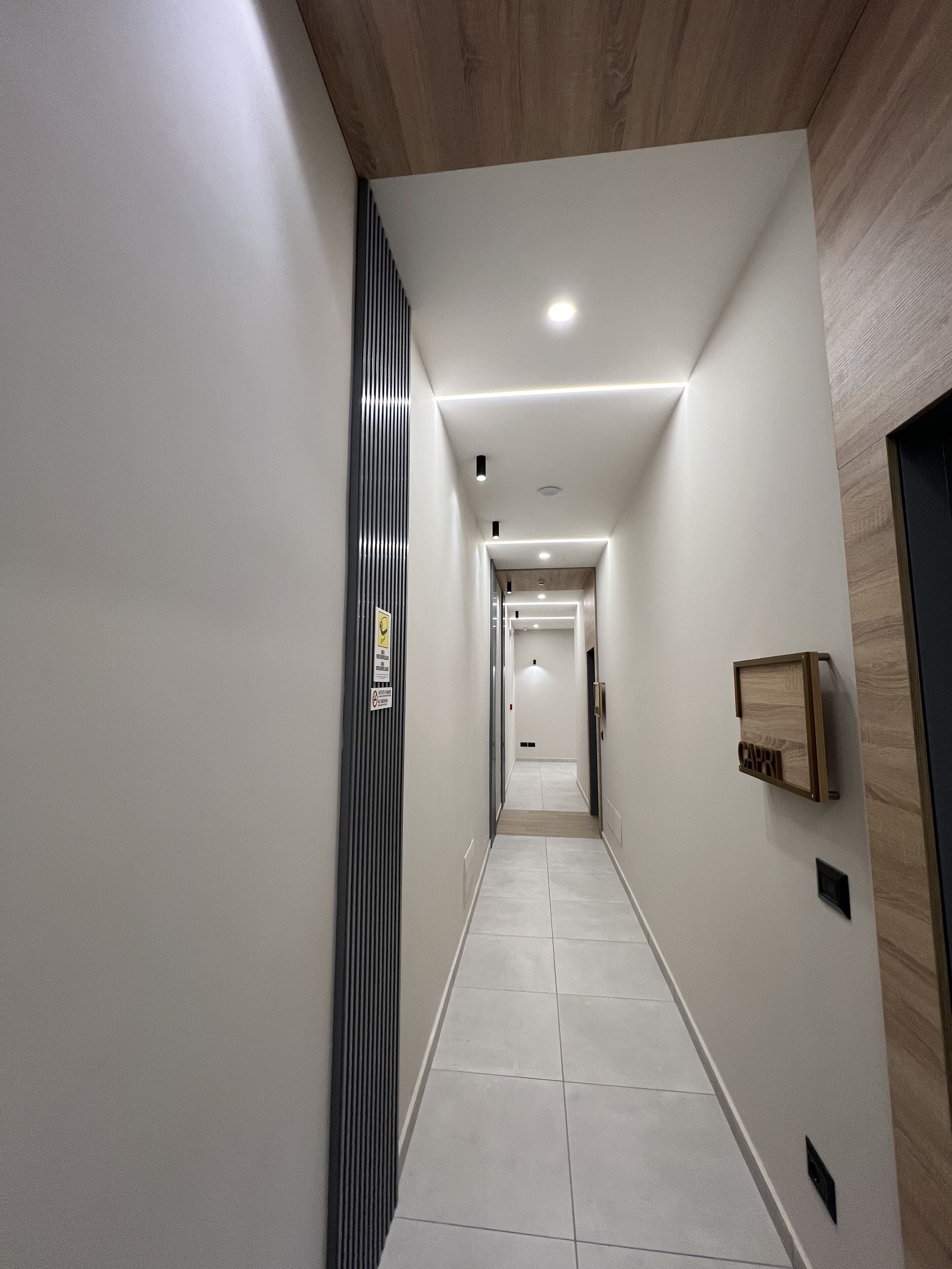 Un corridoio moderno con soffitto in legno, pareti bianche e pavimento piastrellato.