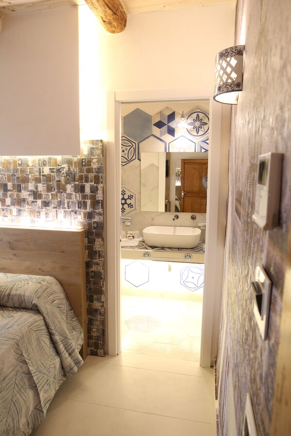 A bathroom with a mosaic tile wall, a wooden bench, a sink, and a mirror. - Relais Piazza del Plebiscito (Naples)