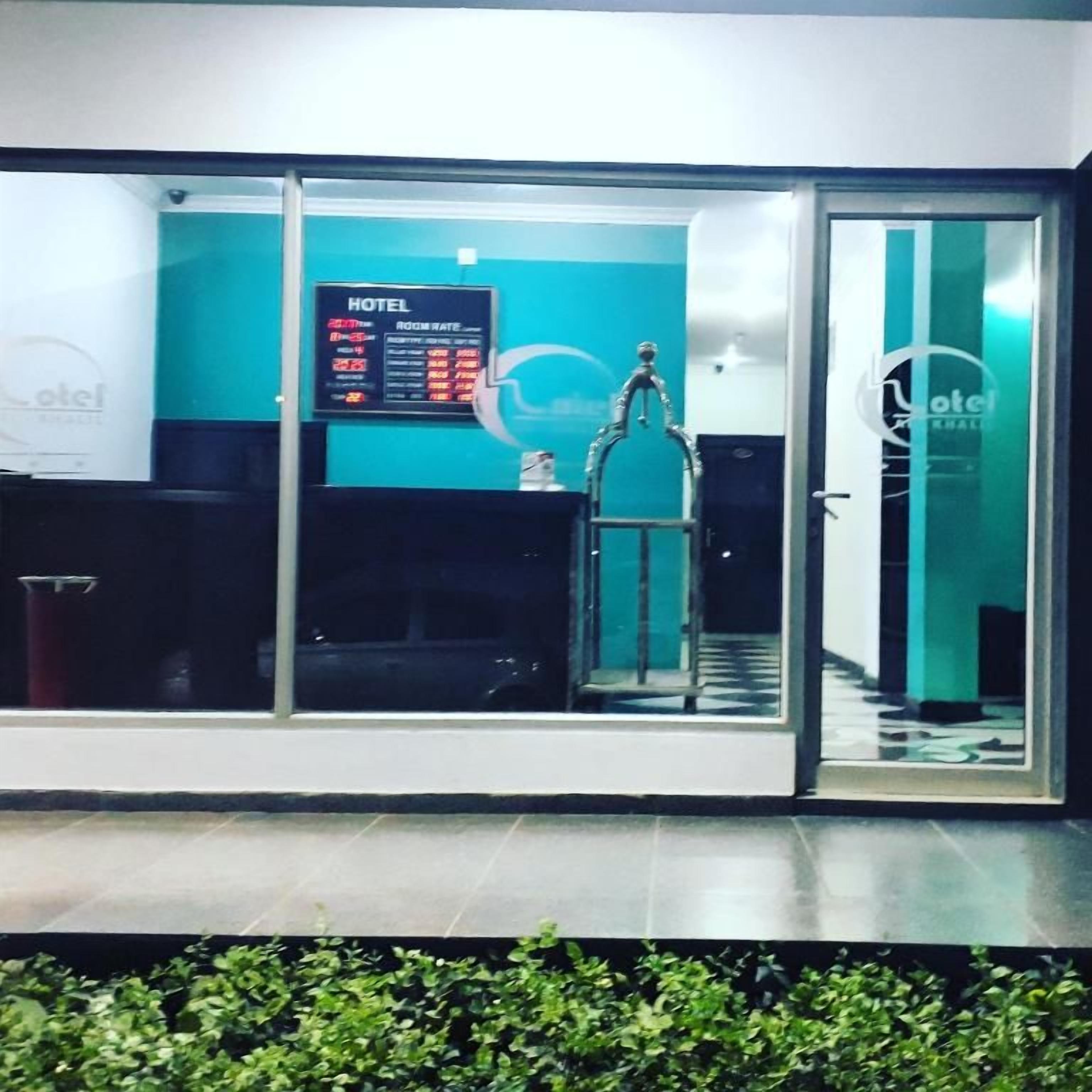 A hotel reception area with a glass door, a reception desk, and a digital display board.