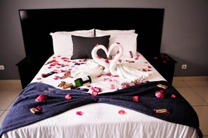 A bed with a heart-shaped towel arrangement, scattered rose petals, and various snacks. - Hotel Al-Khalil (Matola)