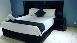 A neatly made bed with white linens and a dark headboard, accompanied by a matching nightstand. - Hotel Al-Khalil (Matola)