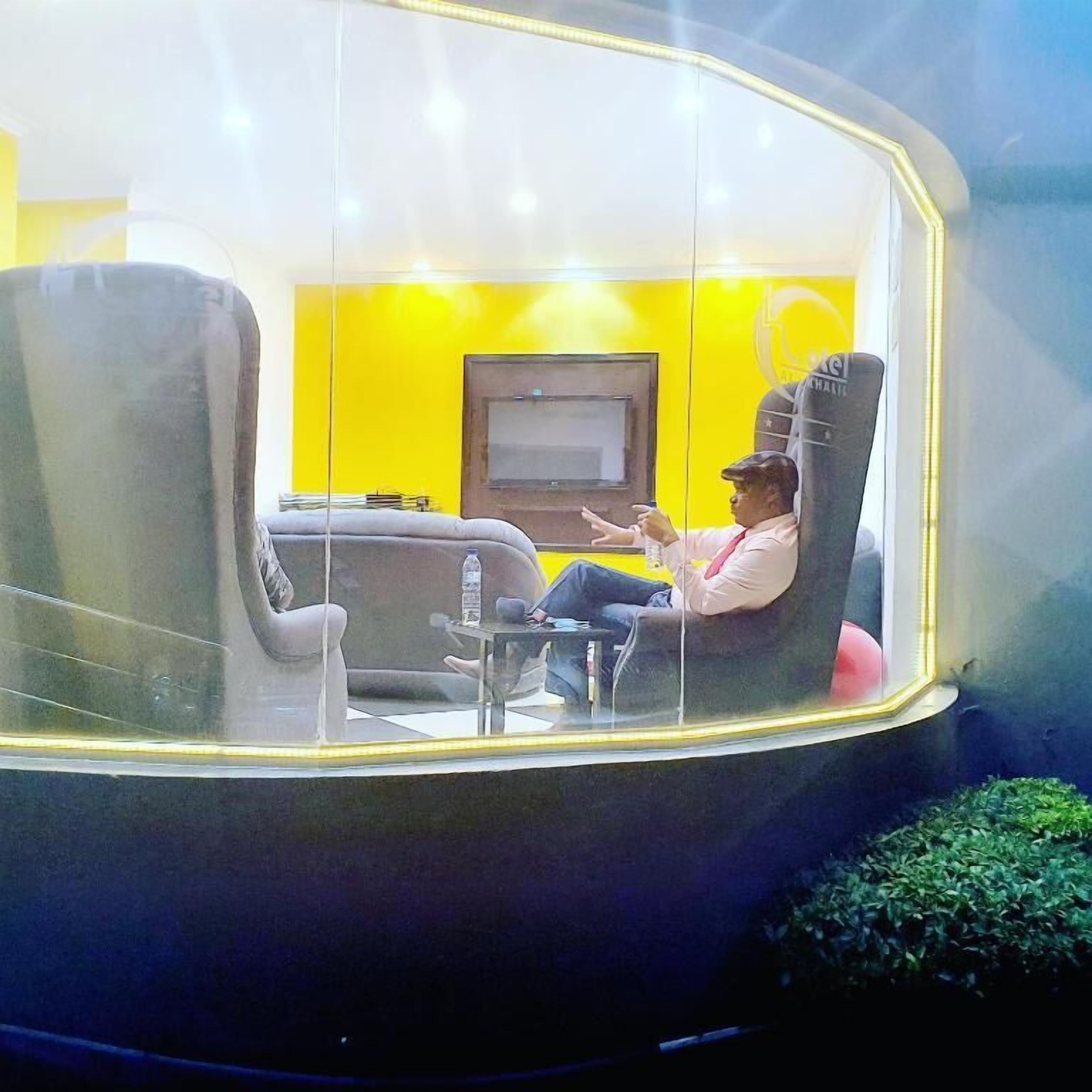 A room with a yellow wall, a flat-screen TV, and a person sitting in a chair.