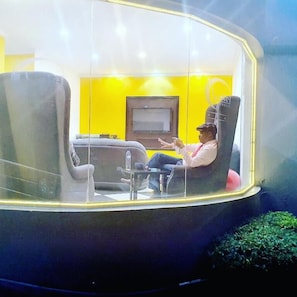 A room with a yellow wall, a flat-screen TV, and a person sitting in a chair. - Hotel Al-Khalil (Matola)
