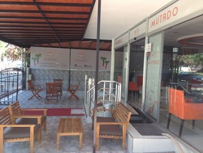 A covered outdoor seating area with wooden benches and tables, a metal railing, and a glass storefront with the sign "MUTADO". - Mutado Hotel (Antalya)