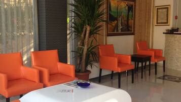 A modern lobby with orange chairs, a white coffee table, a large potted plant, and a painting on the wall.