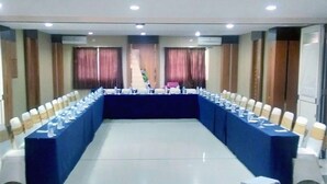 Une salle de conférence avec une longue table, des chaises et un projecteur posé sur un support.