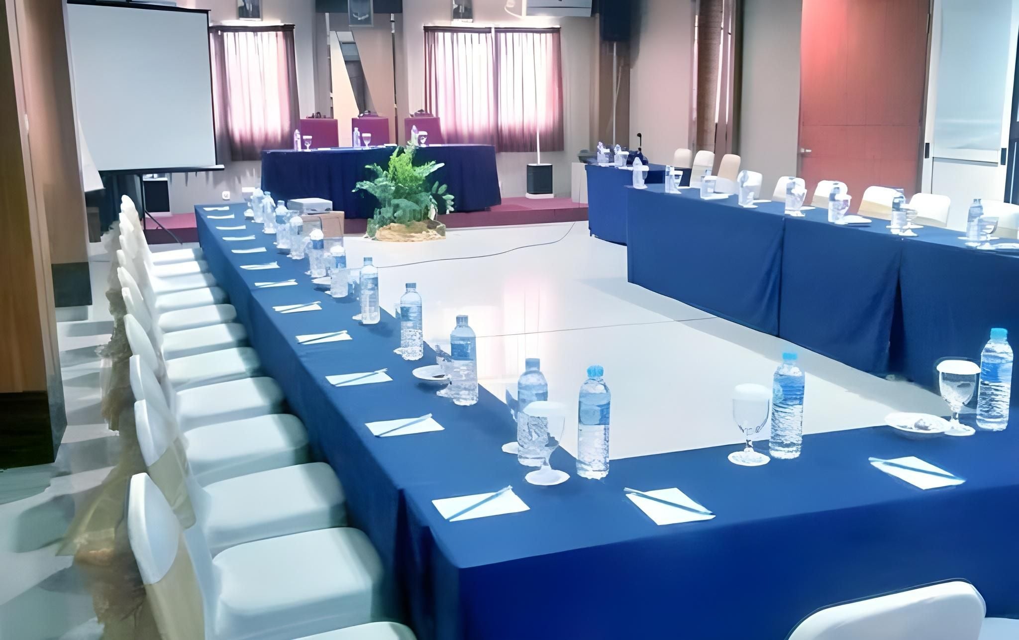 Une salle de conférence avec une longue table préparée pour une réunion, équipée de bouteilles d’eau et de verres.