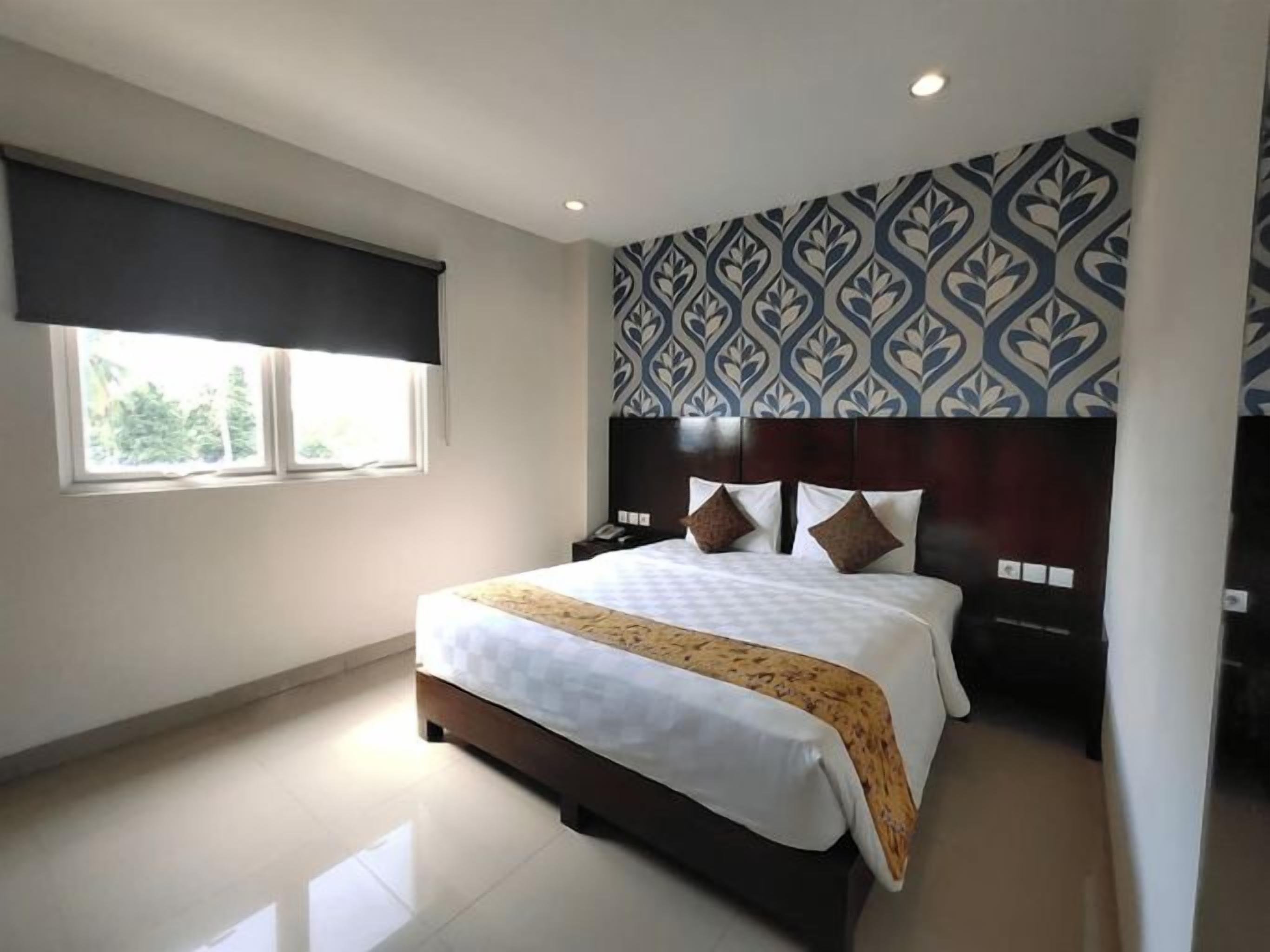 A modern bedroom with a large bed, a headboard, a bedside table, and a window with a blind.