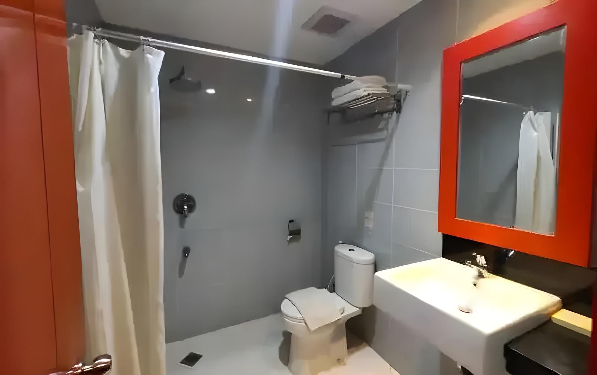 A bathroom with a shower, toilet, and sink, featuring a red-framed mirror and a white curtain.