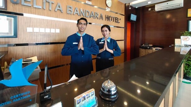 Una mesa de recepción en el Hotel Jelita Bandara, con dos empleados detrás, un reloj y un cartel que indica el nombre del hotel.